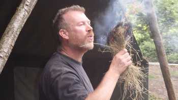 man blowing oxygen into dry grass fire at survival activity camp