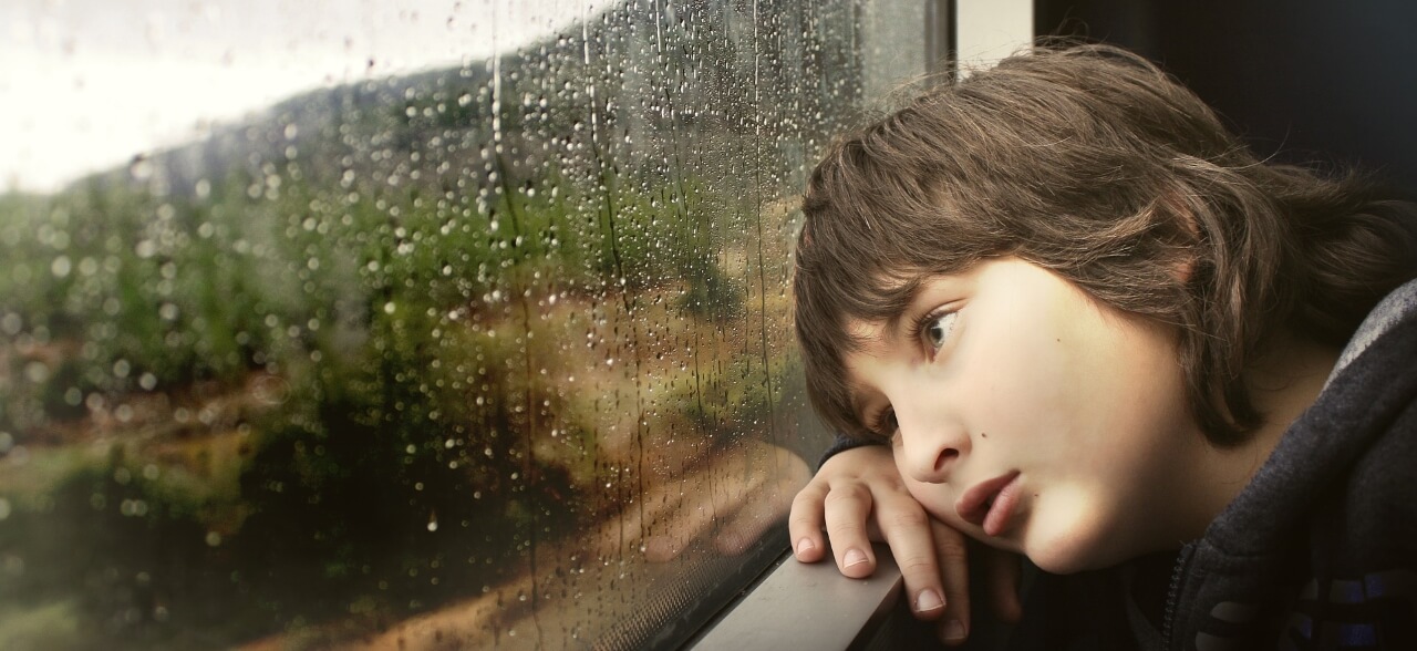 A bored looking child staring out of a rainy window