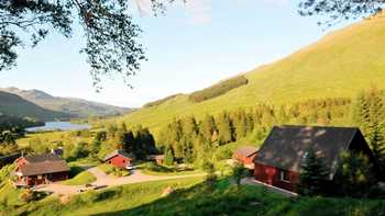 Lodges in Perthshire, Scotland on a hillside in the sunshine with the mountains and lake in the distance