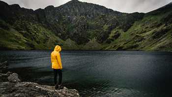 person in raincoat stood looking at lake on a stormy day in Snowdonia, Wales